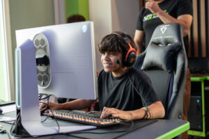 Smiling teenager with a headset plays a video game on a high-end gaming PC at a NextGen tournament.