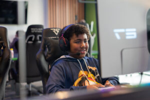 Smiling teenager with a headset plays a video game on a high-end gaming PC at a NextGen tournament.